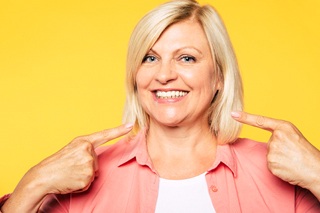 An older woman pointing to her smile