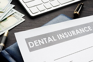 Dental insurance form resting on table near keyboard and money