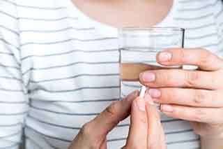 Closeup of hands holding a white pill and a glass of water