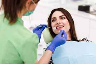 Woman in dental chair smiling at dentist in green scrubs