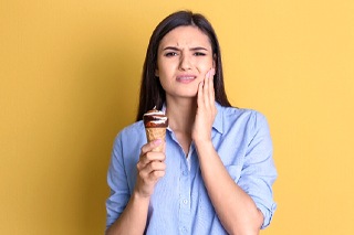A woman touching her cheek in pain while eating ice cream