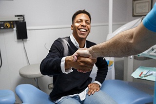 Patient in black sweater smiling while shaking hands with dentist
