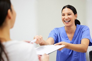 Dental assistant smiling while handing patient form