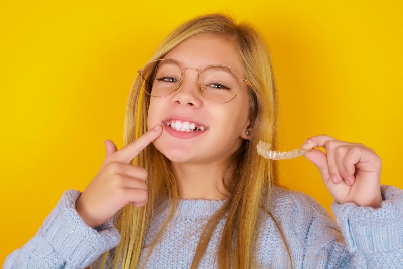 young woman holding her Invisalign aligner against a yellow background