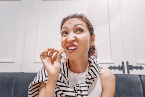 Woman with brown hair in white striped shirt picking her teeth with a toothpick